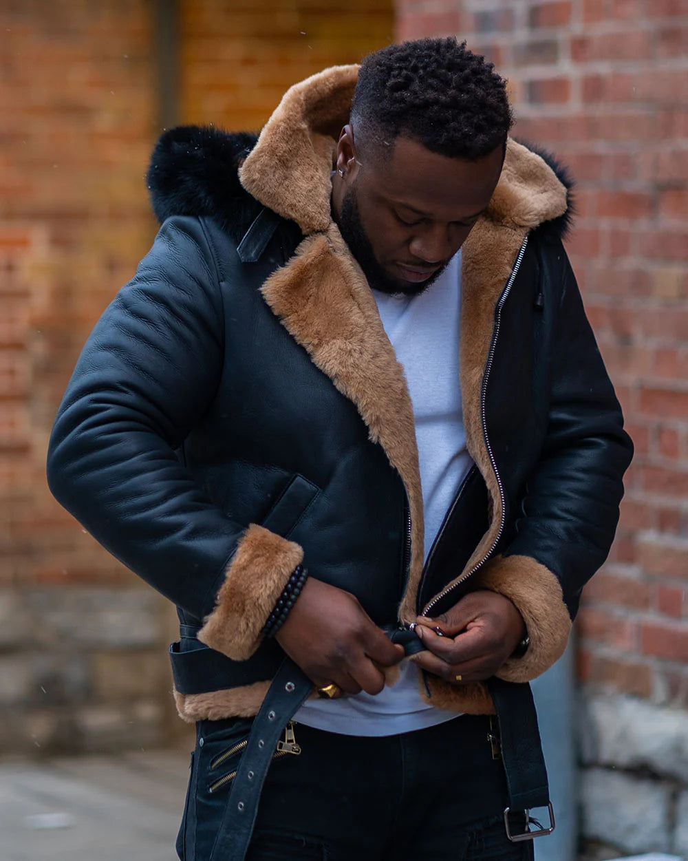 Lifestyle photo of a man adjusting the belt on Jean's B3 Bomber Aviator Shearling Jacket with hoodie, highlighting tan shearling and black leather.