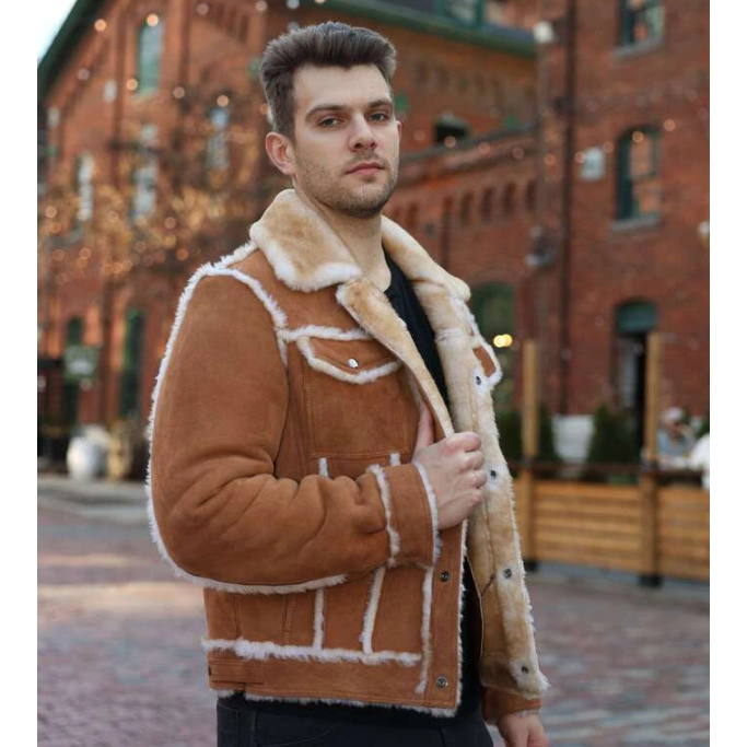Man wearing a brown shearling jacket in an urban setting with brick buildings.