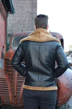 Person wearing a Graysen black Aviator bomber shearling jacket back pose with fur trim standing in front of an old truck.