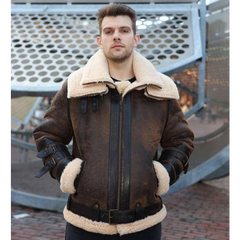 Man wearing a brown leather jacket with white fur lining standing in front of a metal structure.