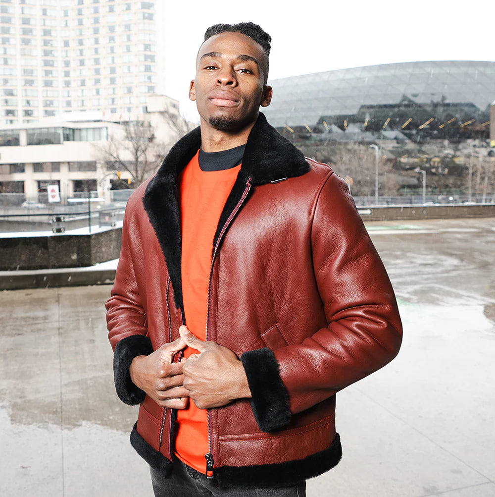 A man wearing the Aurelius Burgundy B3 Bomber Shearling Jacket over an orange shirt in an urban winter setting.
