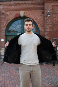 Man wearing Black on Black Belted Shearling Leather Biker Jacket over a white sweater with a brick building background