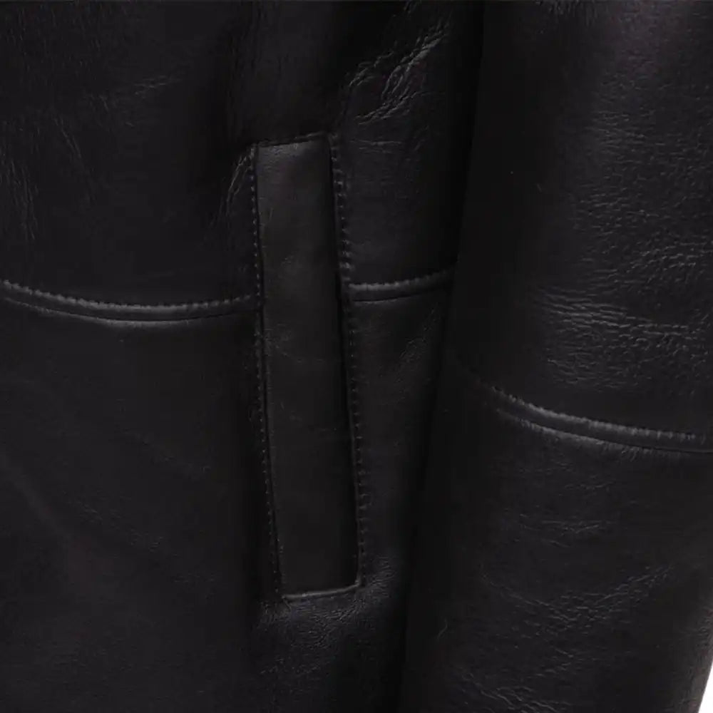Close-up of a black shearling trench coat  pocket with stitching detail.