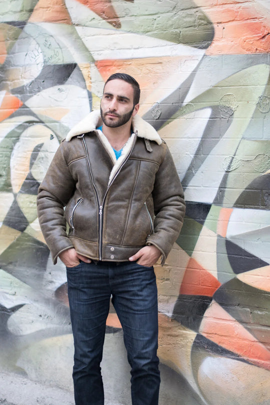Man wearing a distressed biker bomber shearling leather jacket with white fur lining against a colorful mural.