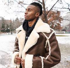 Man wearing a brown shearling overcoat with white fur lining in a snowy outdoor setting