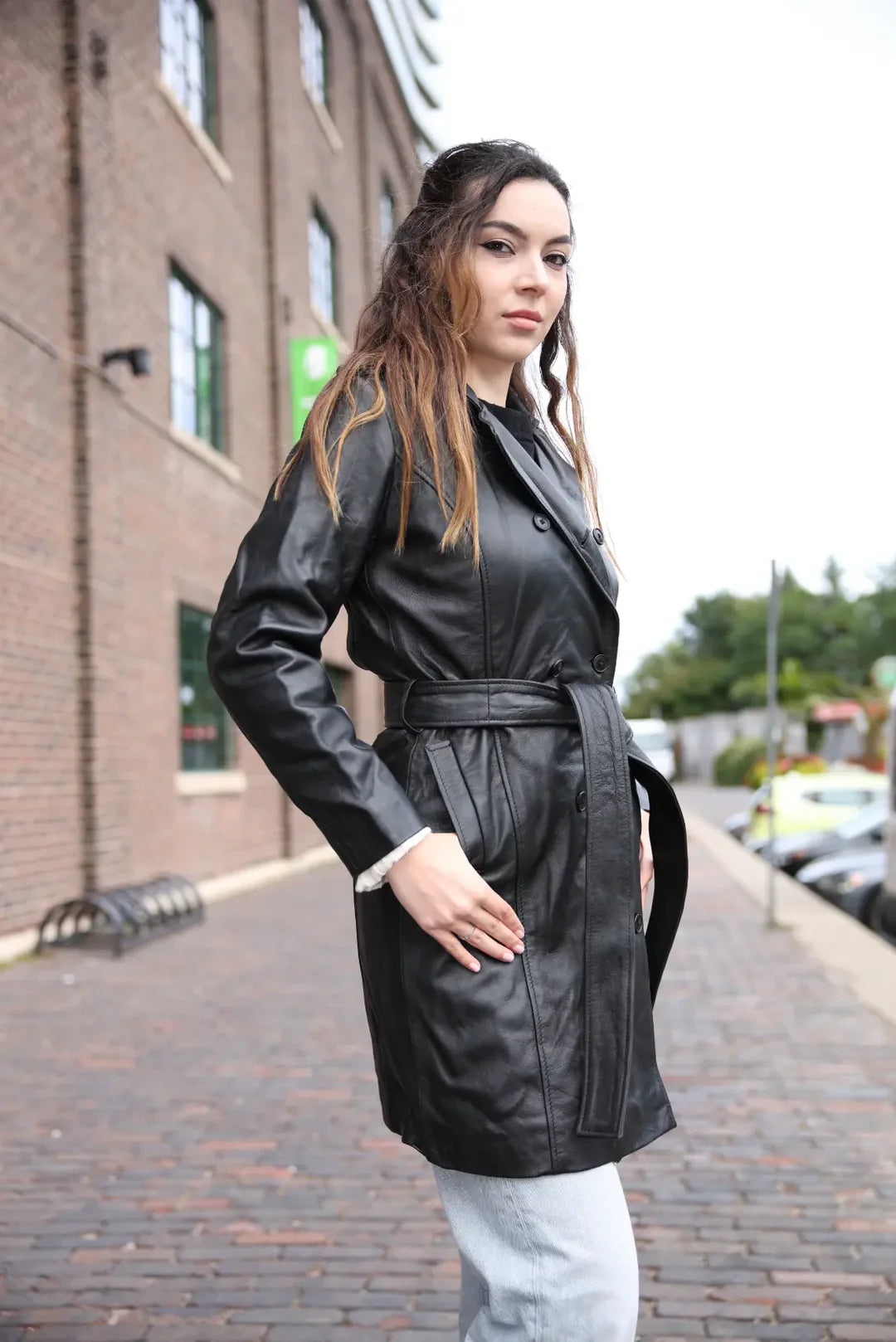 Woman wearing a black leather trench coat on a city street.