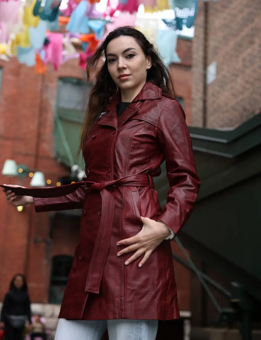 Woman wearing a red leather trench coat in an urban setting with colorful decorations.