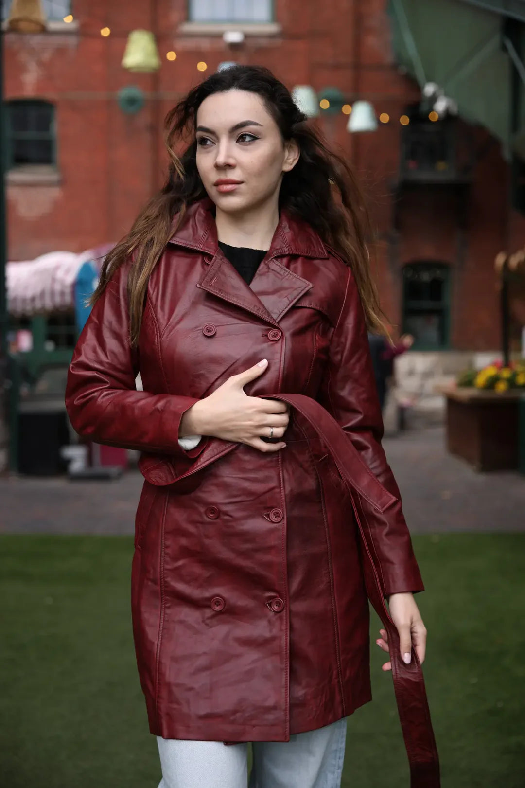 Action shot of a woman while wearing the coral red belted leather coat, showcasing the open belt and rich color of the premium leather.