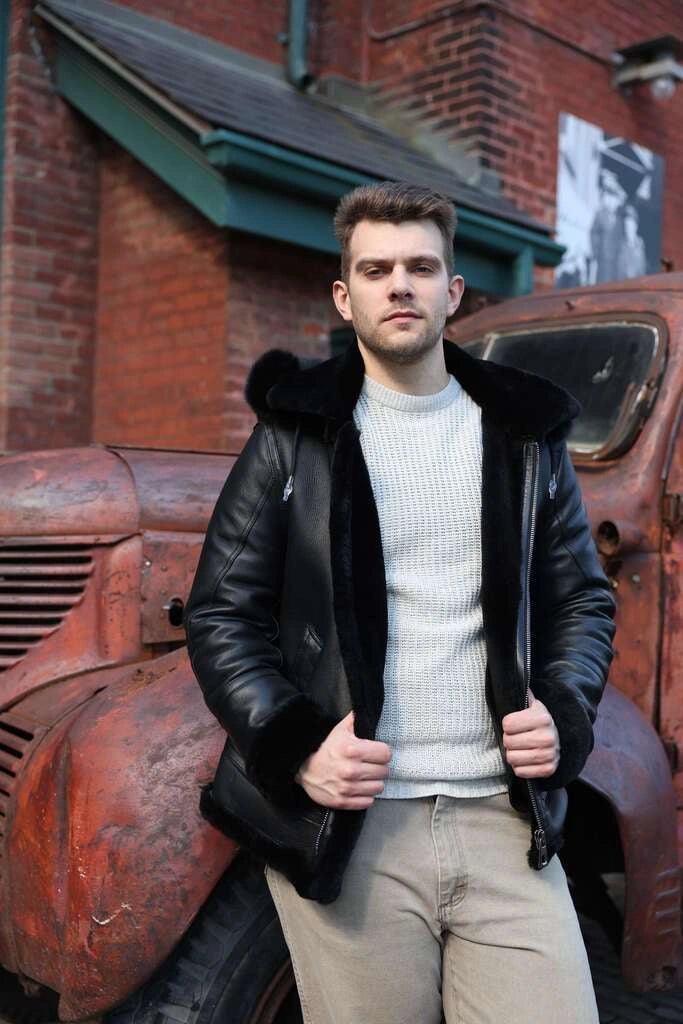 Man wearing Felix black bomber shearling jacket with fur collar standing next to an old red truck.