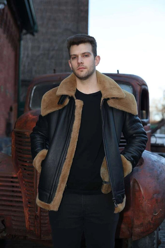 Man wearing Graysen black Aviator bomber shearling jacket with brown fur collar standing in front of an old truck.