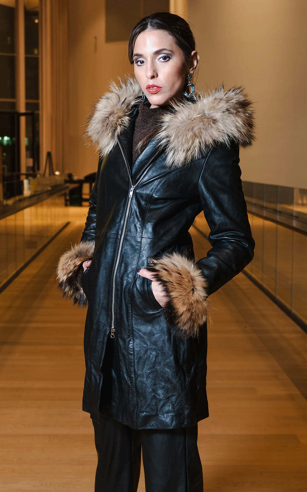 Woman wearing a black leather winter coat with fur trim indoors.