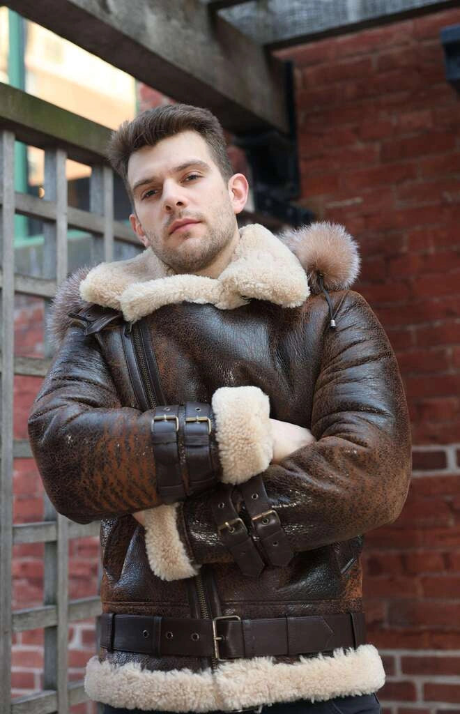Man Rocco vintage brown aviator shearling jacket with fur trim standing against a brick wall with hands closed.