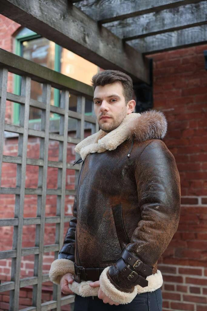 Man wearing Rocco vintage brown aviator shearling jacket with fur trim zips closed standing in front of a brick wall.