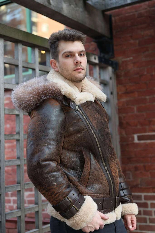 Man wearing a brown leather jacket Rocco vintage brown aviator shearling jacket with fur trim standing against a brick wall.