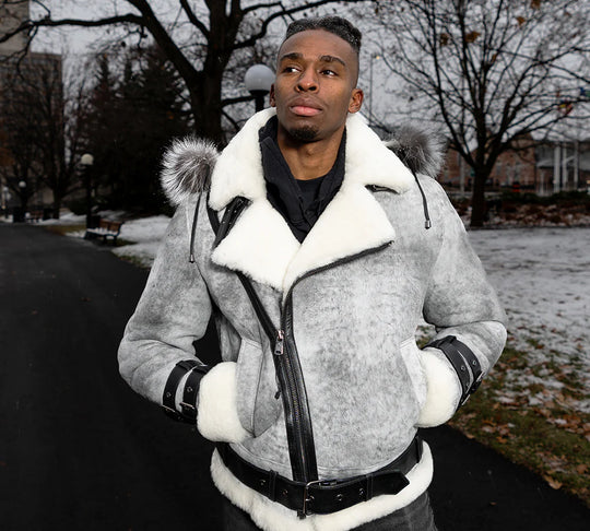 Man wearing a gray aviator shearling aviator bomber jacket with white fur trim outdoors on a snowy day.