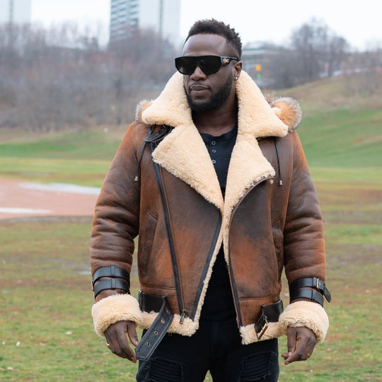 Lifestyle photoshoot of a man wearing Rocco vintage brown aviator shearling jacket with open zipper and waist belt in an outdoor park setting.